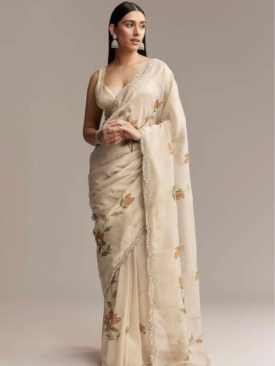 Woman wearing a beige saree with floral patterns on a plain background